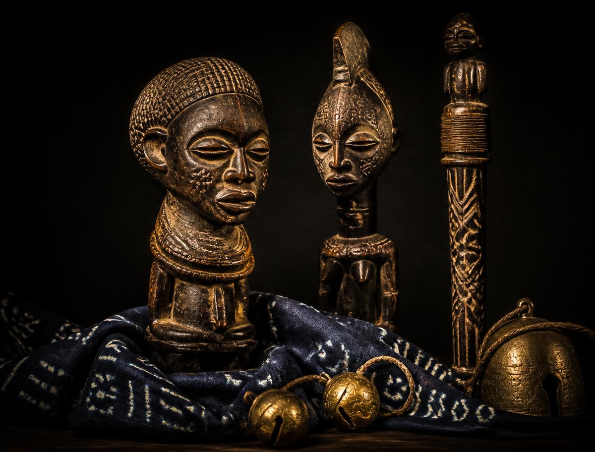 Carved ancestral figures and brass bells on indigo adire cloth